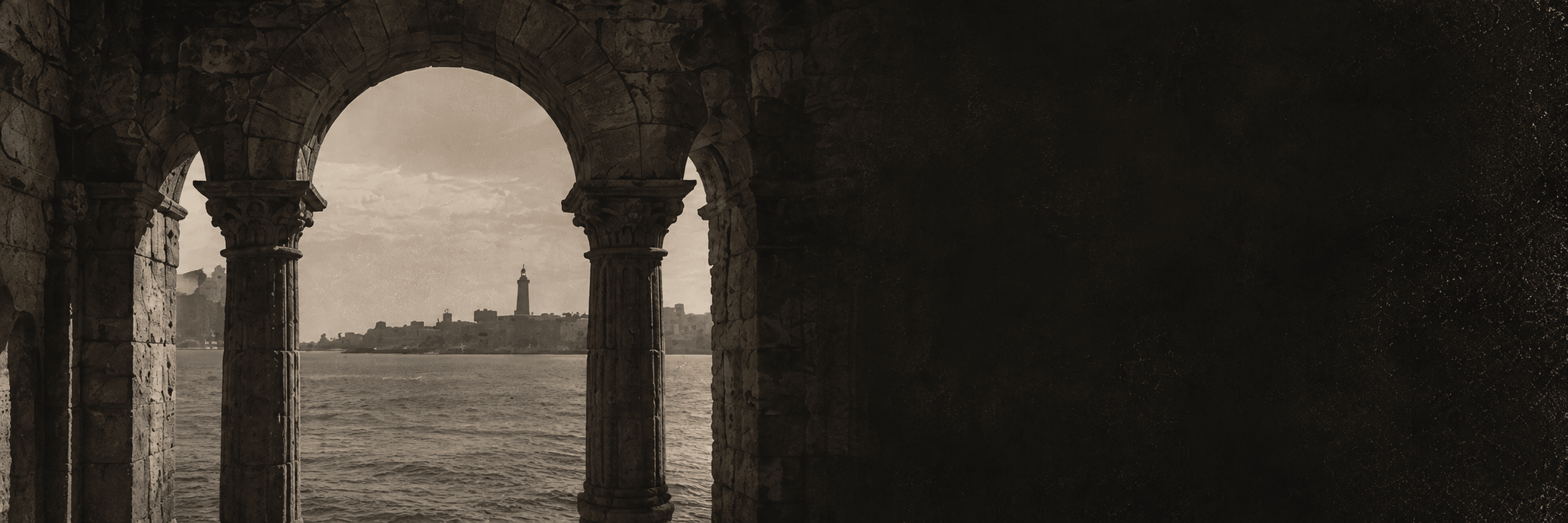 A stone arcade framing the sea and the distant lighthouse of Alexandria